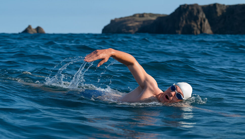 Moški med plavanjem v odprti vodi z očali in plavalno kapo – simbol fizične aktivnosti, povezane s temo kaj jesti pred in po plavanju.